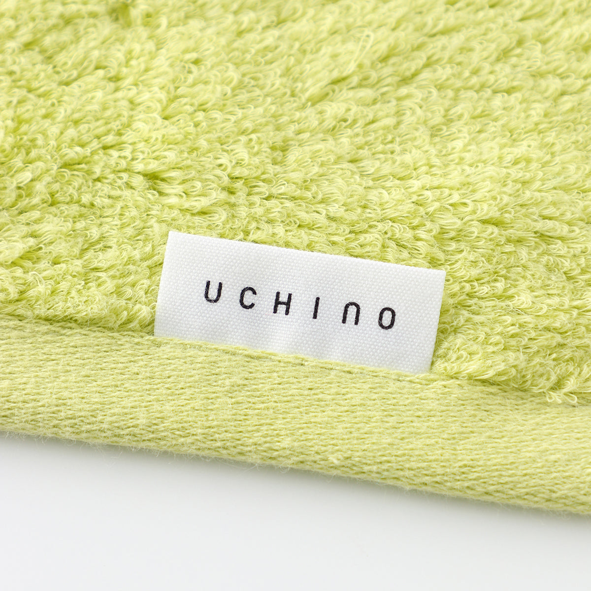 Close-up of the pile and hem band of a pale green UCHINO towel, with the woven label