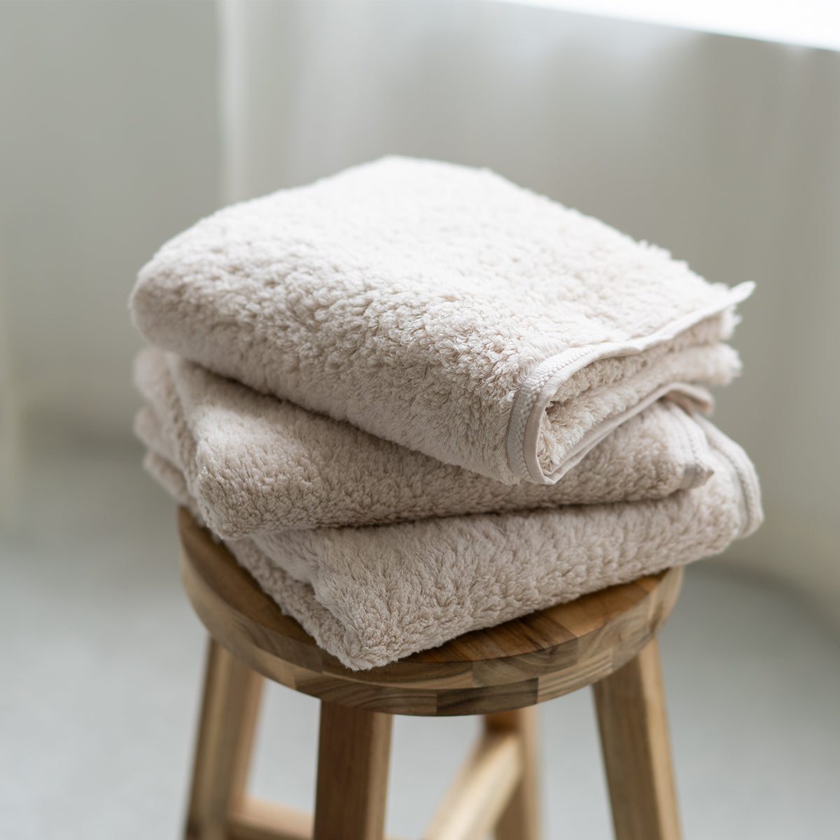 Three folded cotton towels stacked on a wooden stool in soft daylight